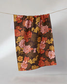 Mabel tea towel in chocolate brown with coral, pink, and golden retro floral print hanging on a line