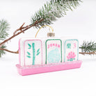 Hand-painted mahjong tile glass ornament with a Joker tile hanging on an evergreen branch
