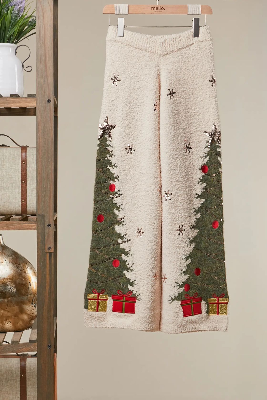 Ivory plush knit wide-leg sweater pants with green Christmas trees, snowflakes, and red gift box details on a hanger