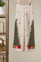 Ivory plush knit wide-leg sweater pants with green Christmas trees, snowflakes, and red gift box details on a hanger