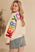Ivory oversized knit Christmas sweater with multicolor Merry Christmas lettering across the back and sleeves, styled with denim shorts