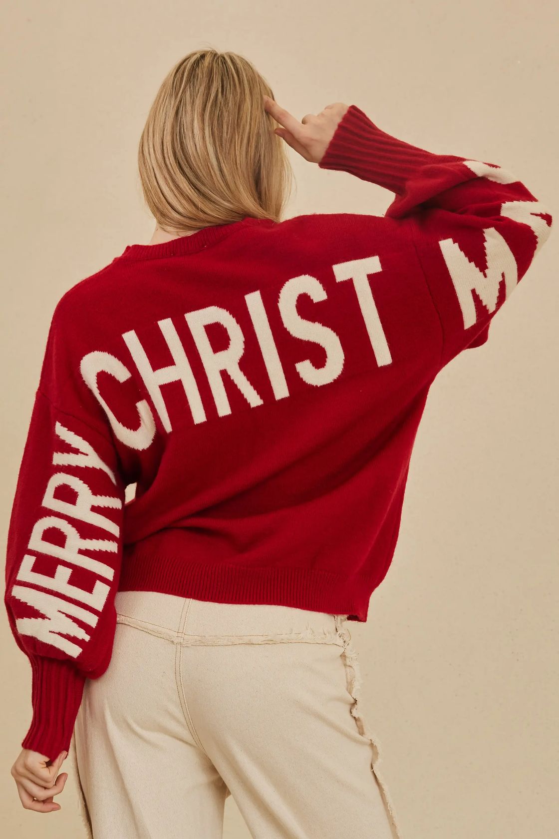 Red oversized knit sweater with ivory Merry Christmas lettering across the back and sleeves, styled with cream trousers