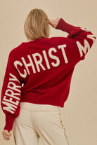 Red oversized knit sweater with ivory Merry Christmas lettering across the back and sleeves, styled with cream trousers