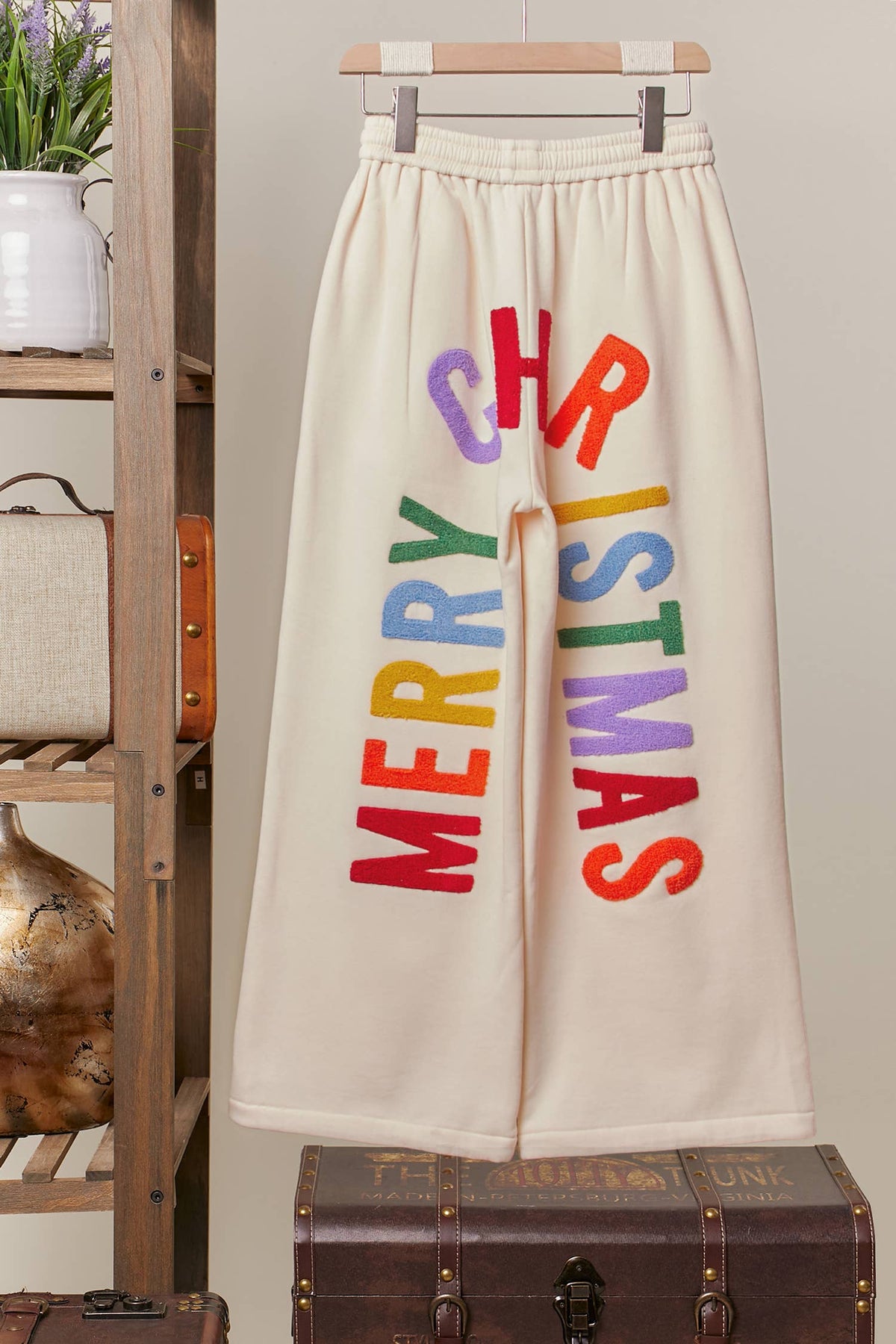 Back of the cream wide-leg sweatpants with arched multicolor Merry Christmas lettering, on a hanger