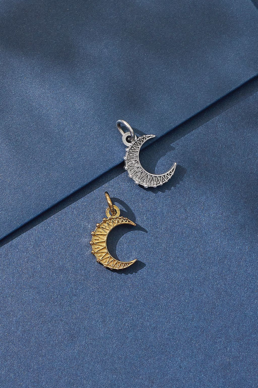 Two moon-shaped pendants, one gold and one silver, on a blue fabric background.