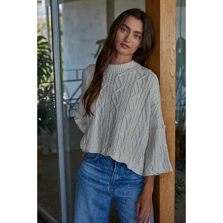Natural cream cable-knit cotton pullover sweater with a crew neck and wide three-quarter sleeves, worn with blue jeans