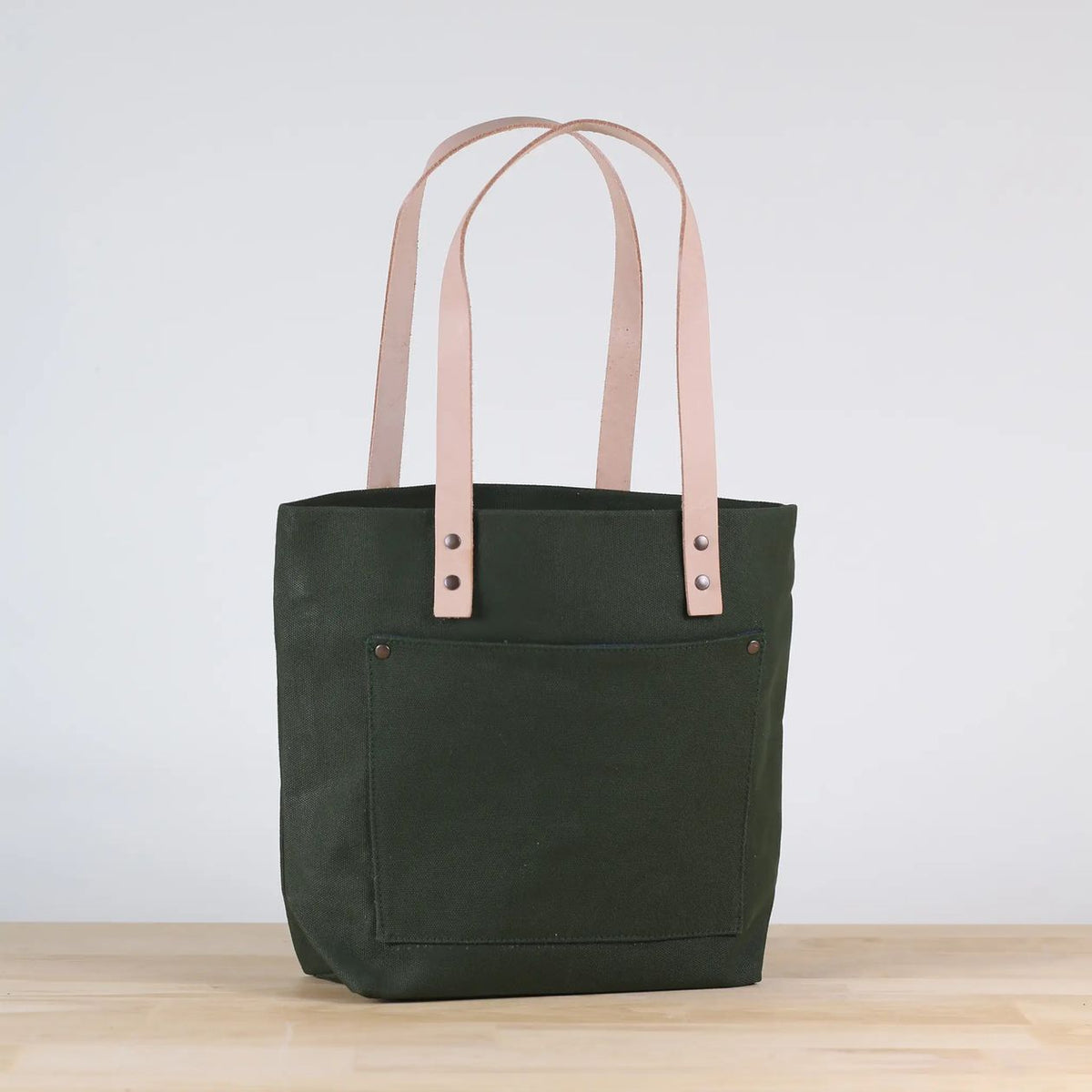 Green tote bag with pink straps on a light wooden surface and white background