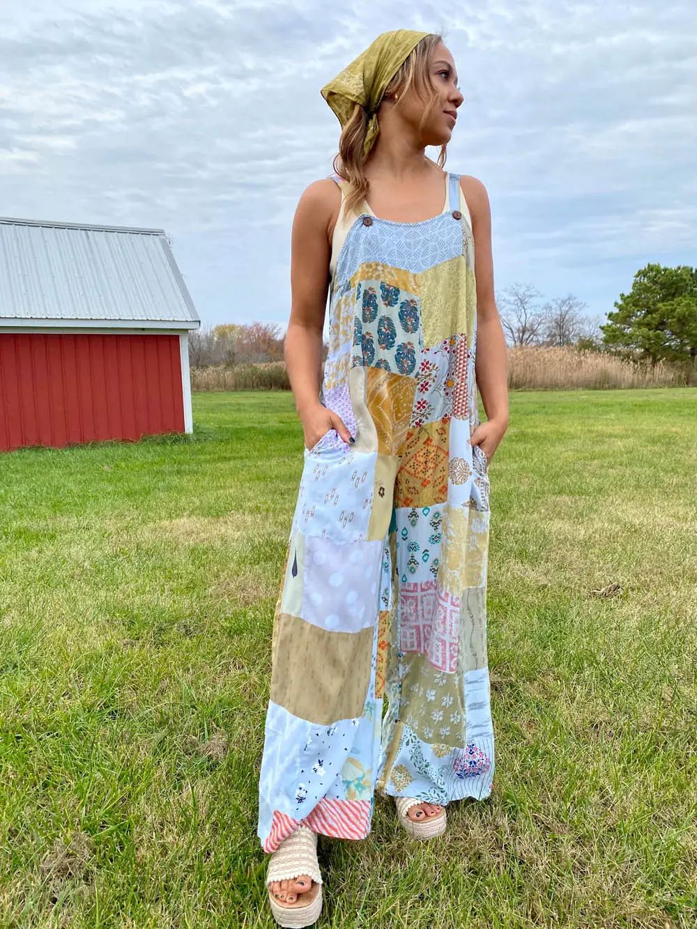 Woman wearing a patchwork dress standing in a grassy field with a barn in the background