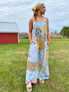Woman wearing a patchwork dress standing in a grassy field with a barn in the background