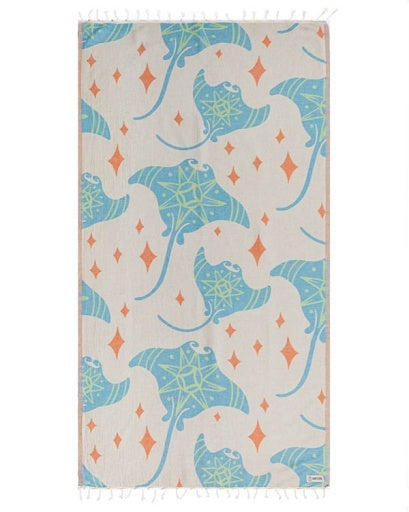 A rectangular beach towel with fringed edges, featuring a pattern of blue stingrays and orange diamond shapes on a light beige background.