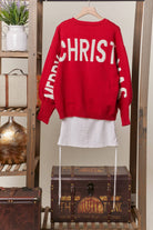 Back of the red sweater on a hanger showing ivory Merry Christmas lettering across the back and sleeves