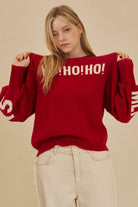 Model wearing the oversized Red Merry Christmas Sweater with ivory HO HO HO lettering on the front and cream trousers