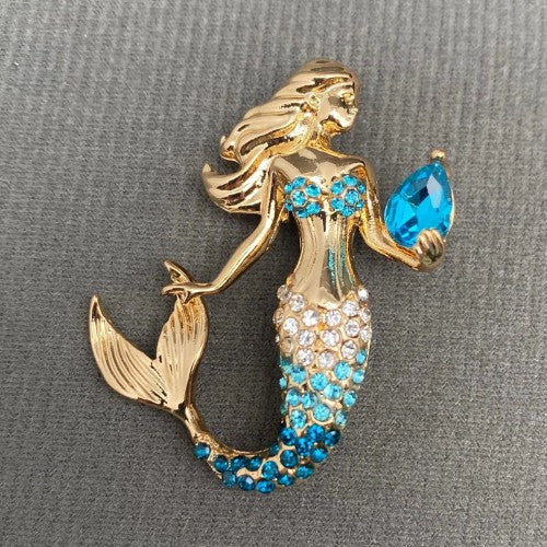Gold mermaid brooch with blue gemstones on a gray background