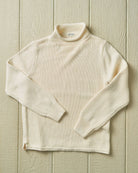 Cream-colored ribbed knit sweater on a wooden surface