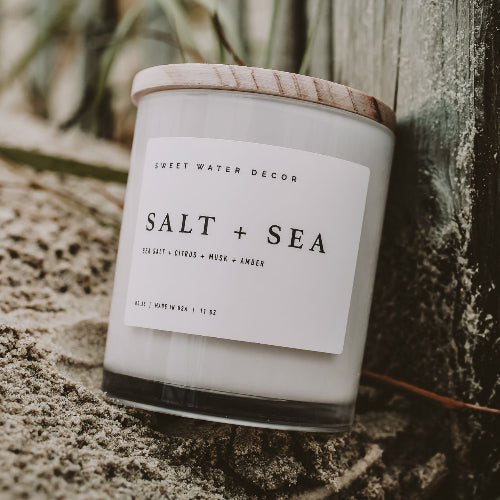 Candle labeled 'Salt + Sea' by Sweet Water Decor on a textured surface.