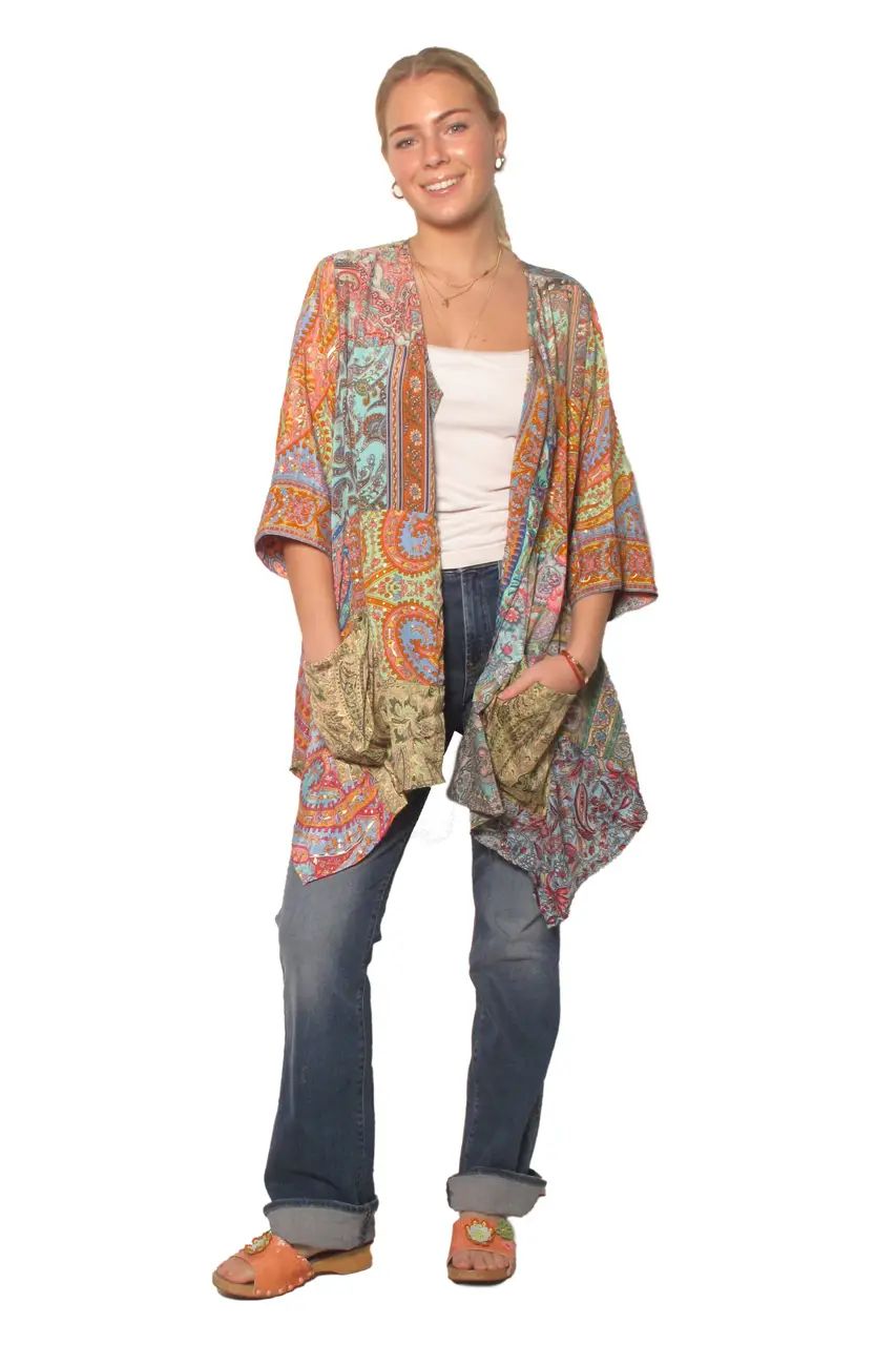 A woman modeling a lightweight, open-front kimono cardigan with a vibrant multicolor paisley pattern, styled over a white tank top, blue jeans, and brown sandals against a plain white background.