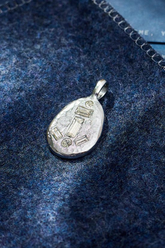 Silver pendant on a blue textured fabric background