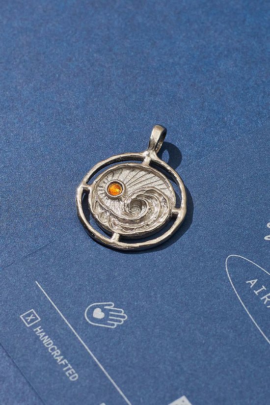 Silver pendant with a red gemstone on a blue background