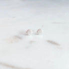A pair of small silver stud earrings shaped like scallop shells, resting on a light marble surface.