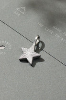 Silver star-shaped pendant on a textured gray surface with text.