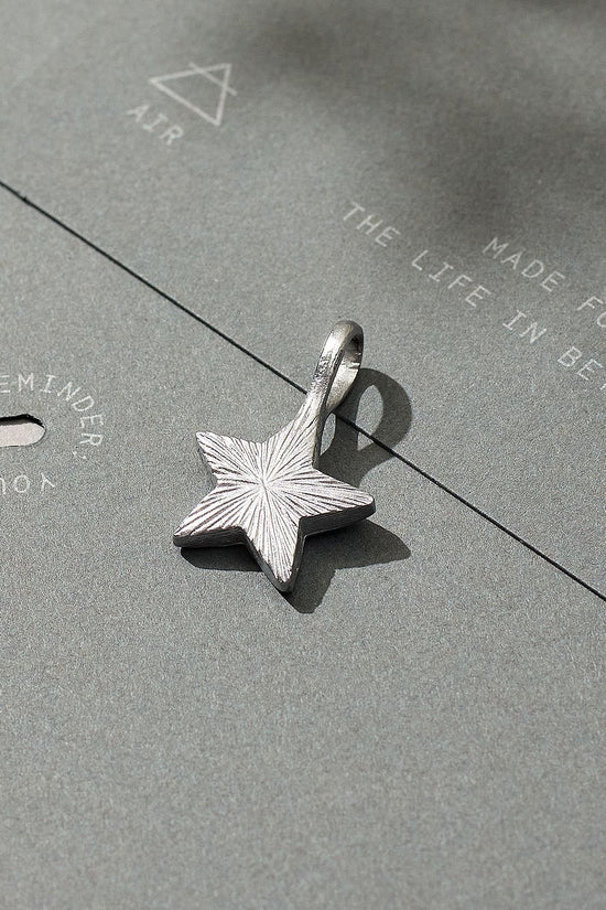 Silver star-shaped pendant on a textured gray surface with text.