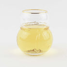 Snowman shaped drinking glass with gold rim filled with white wine on a white background