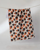 Squirrel Bounty tea towel in soft cream with orange, brown, and charcoal acorn print hanging on a line