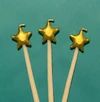 Three gold star-shaped toppers on wooden sticks, set against a solid teal-green background.