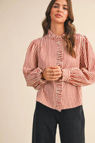 Woman wearing the &merci Striped Ruffle Blouse in red and cream stripes with a ruffled high neck and puff sleeves, front view