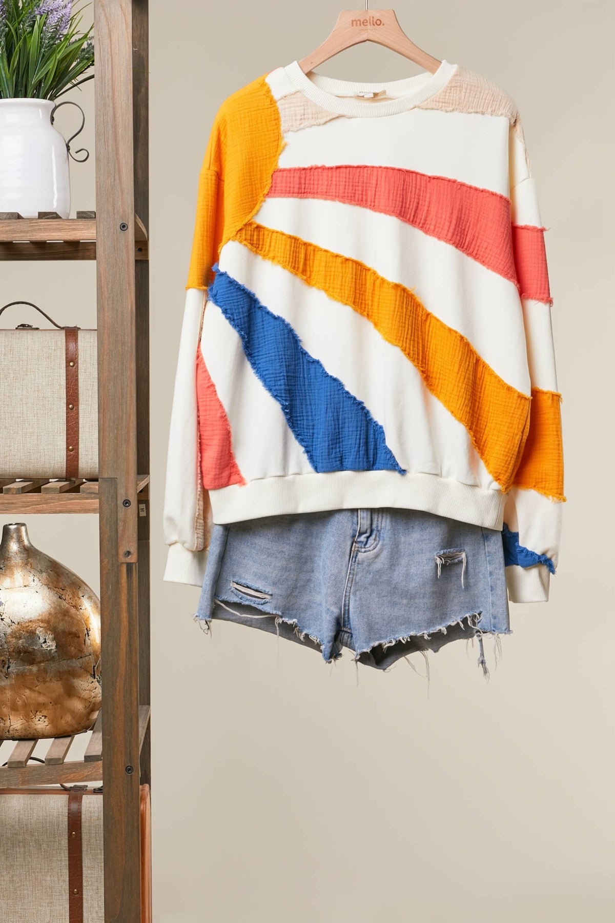 Front view of the ivory Sun Patchwork Sweatshirt with diagonal coral, blue, and marigold stripes, styled with denim shorts
