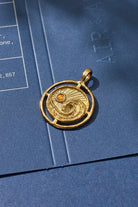 Gold pendant with a circular design on a blue surface