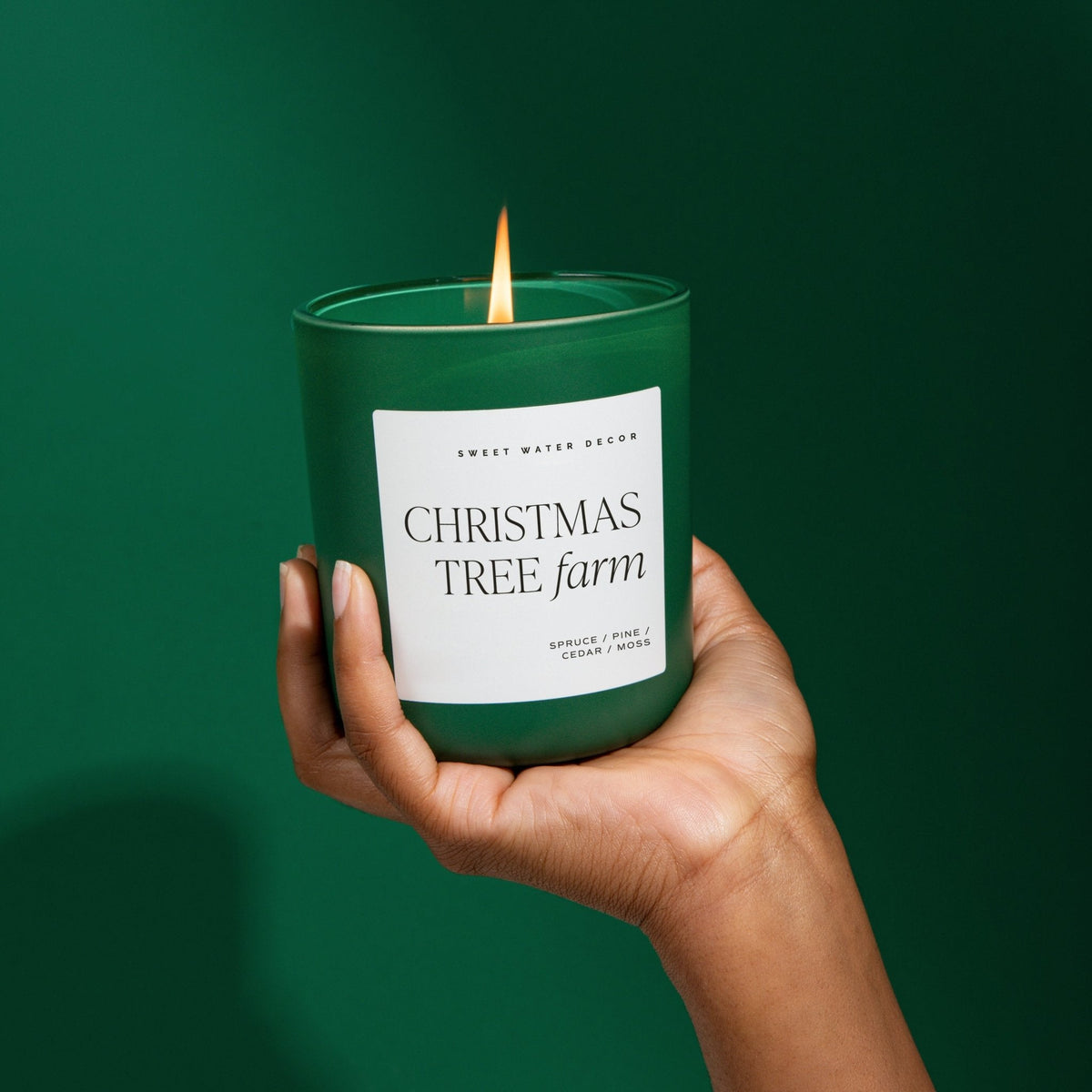 Hand holding the lit Christmas Tree Farm green matte soy candle