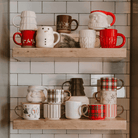 Sweet Water Decor holiday figurine mugs including the Cream Tree mug on a kitchen shelf