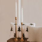 Cream tree-shaped taper candles in brass candlesticks styled for the holidays