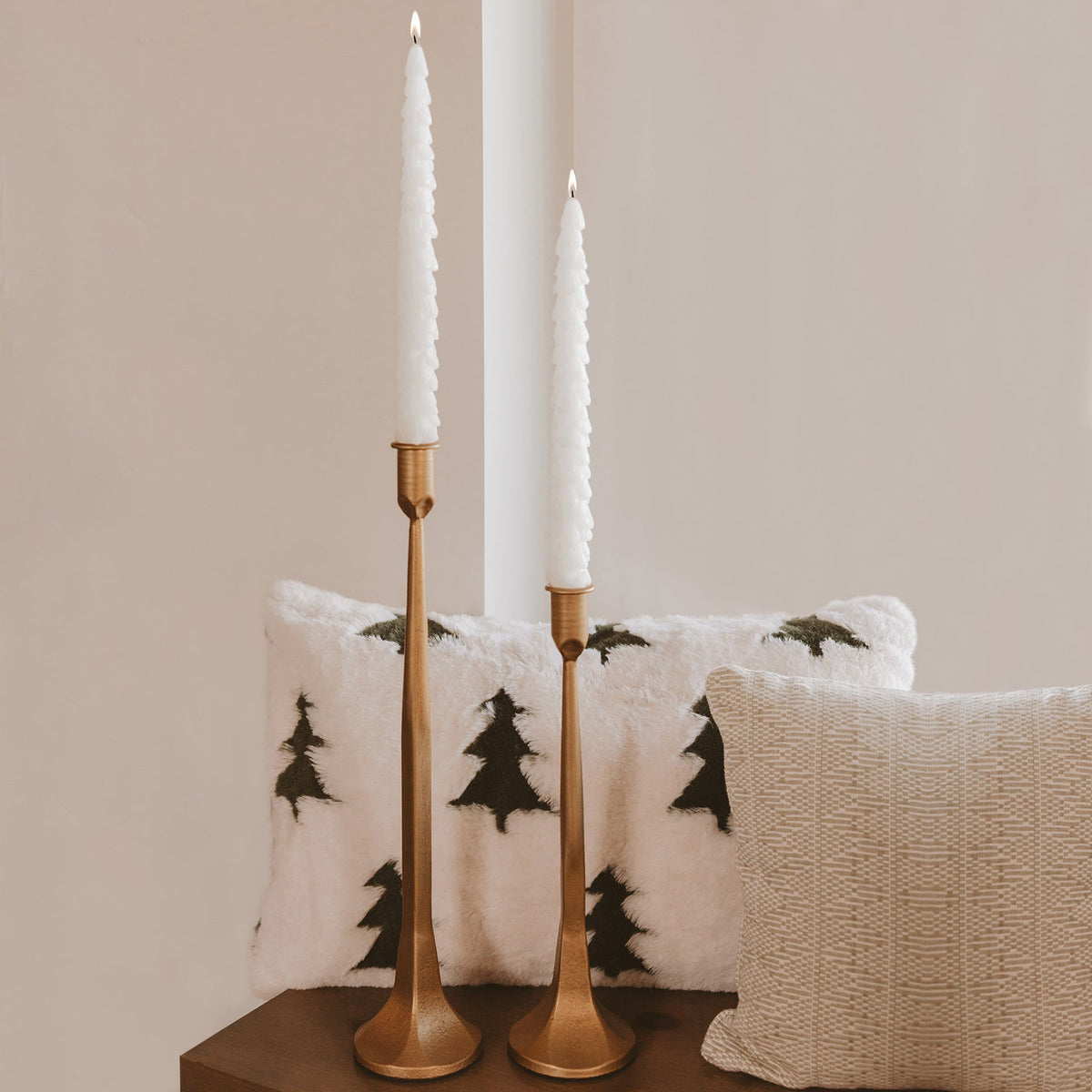 Cream tree-shaped taper candles in brass candlesticks styled for the holidays