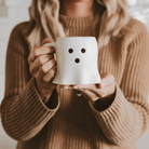 Woman in a knit sweater holding the white Ghost coffee mug