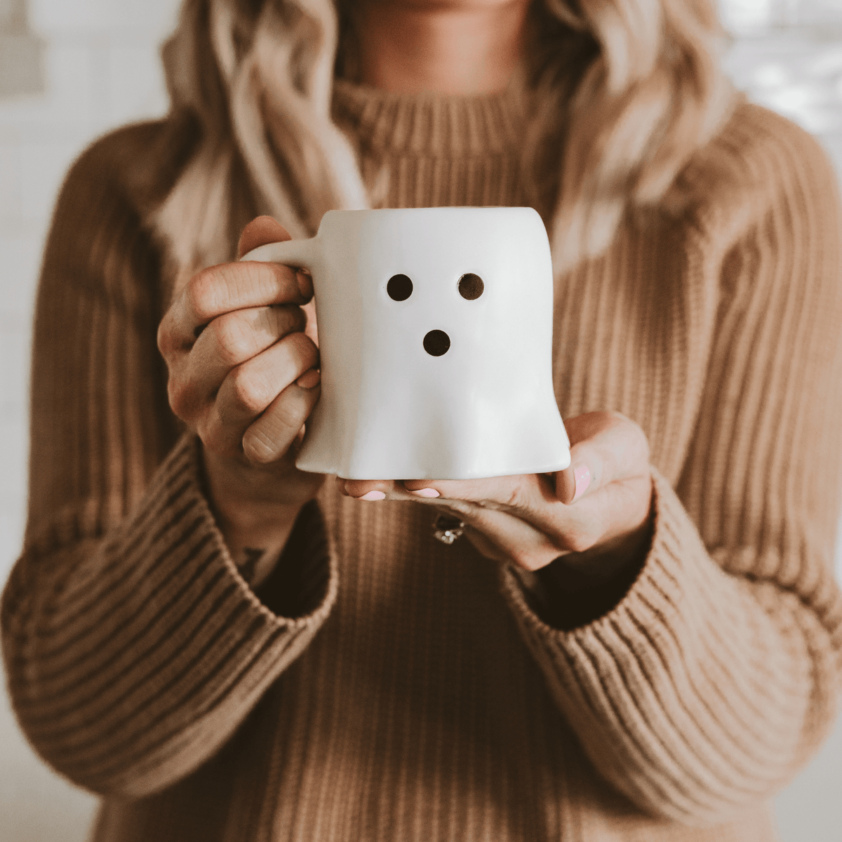 Woman in a knit sweater holding the white Ghost coffee mug