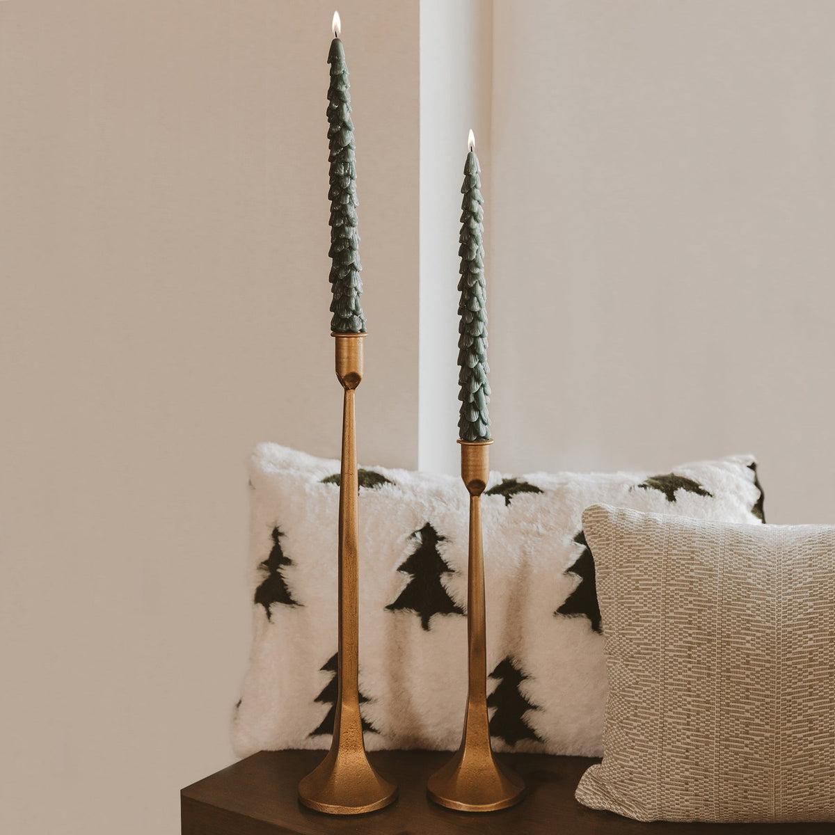 Green tree taper candles in brass candlesticks styled on a holiday mantel