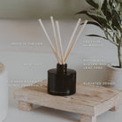 Hello Fall amber reed diffuser on a wooden riser with greenery