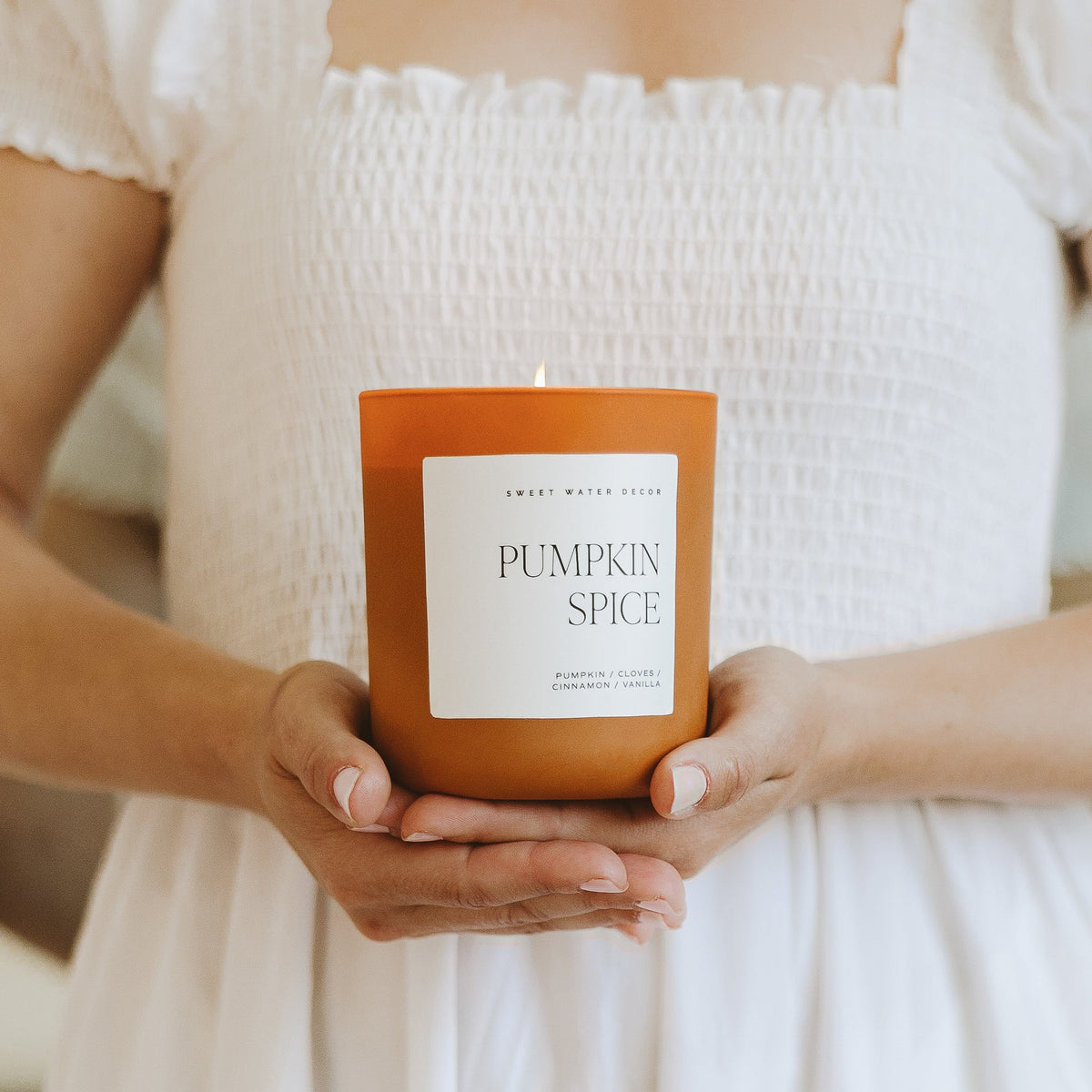 Woman holding the Pumpkin Spice 15 oz soy candle in an orange matte jar