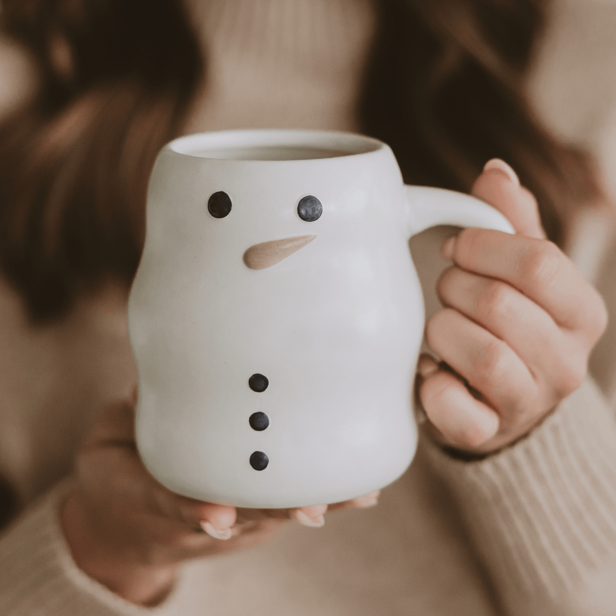 Hands holding the white ceramic Snowman coffee mug with a wood-tone carrot nose