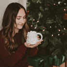 Woman holding the white Santa face coffee mug by a Christmas tree