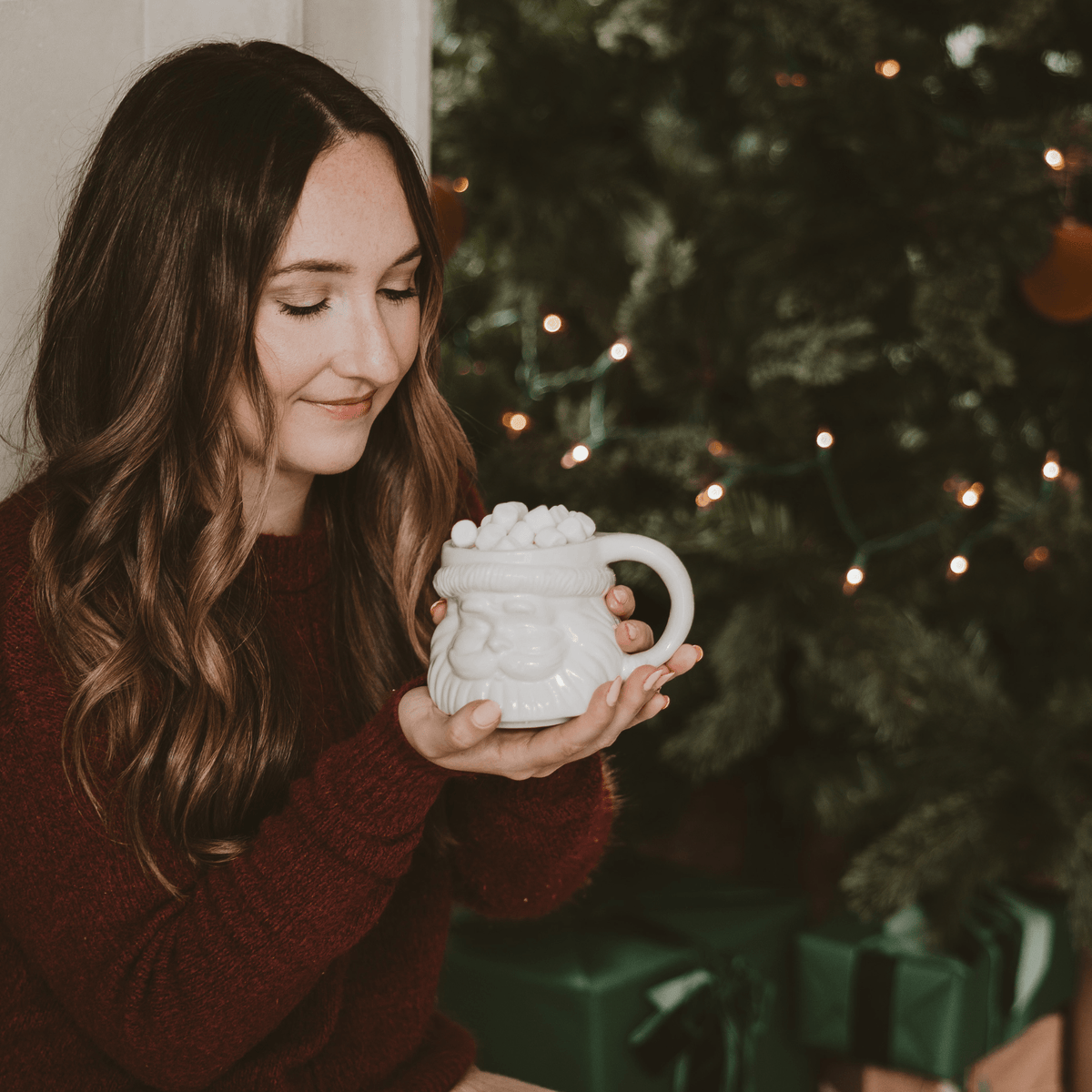 Woman holding the white Santa face coffee mug by a Christmas tree