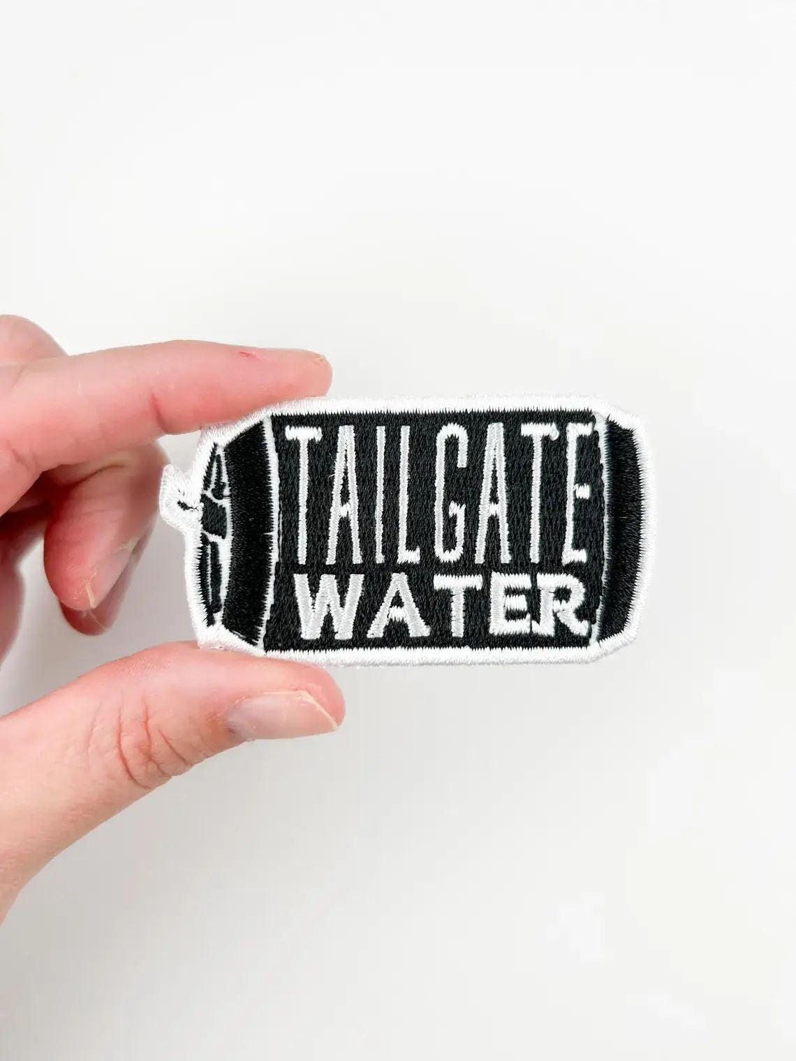 Hand holding a 'Tailgate Water' patch against a white background