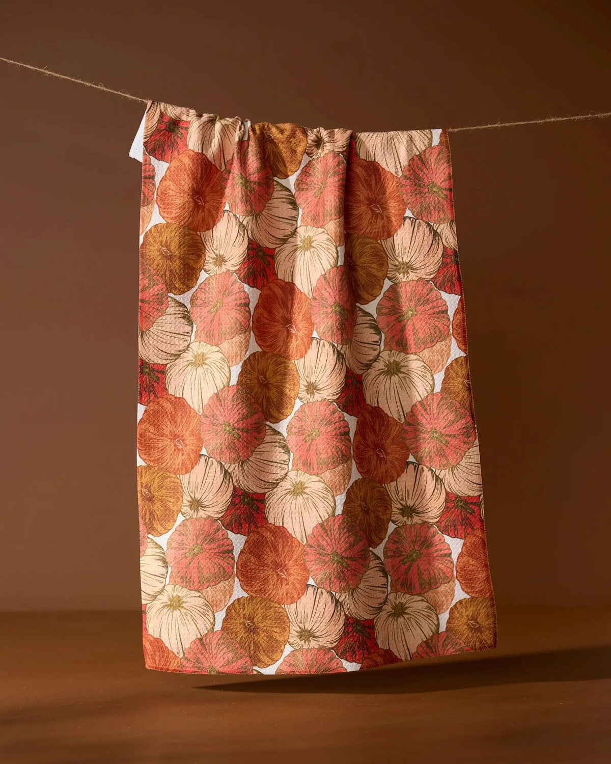 Tendril tea towel with coral, rust, cream, and gold pumpkin print hanging on a line