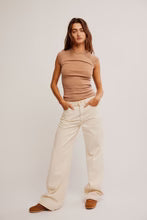 A woman modeling a sleeveless ribbed beige top and cream wide-leg pants against a plain beige studio background.