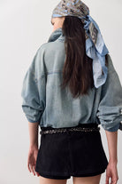Back view of black vegan suede micro skort worn with an oversized chambray shirt and studded belt