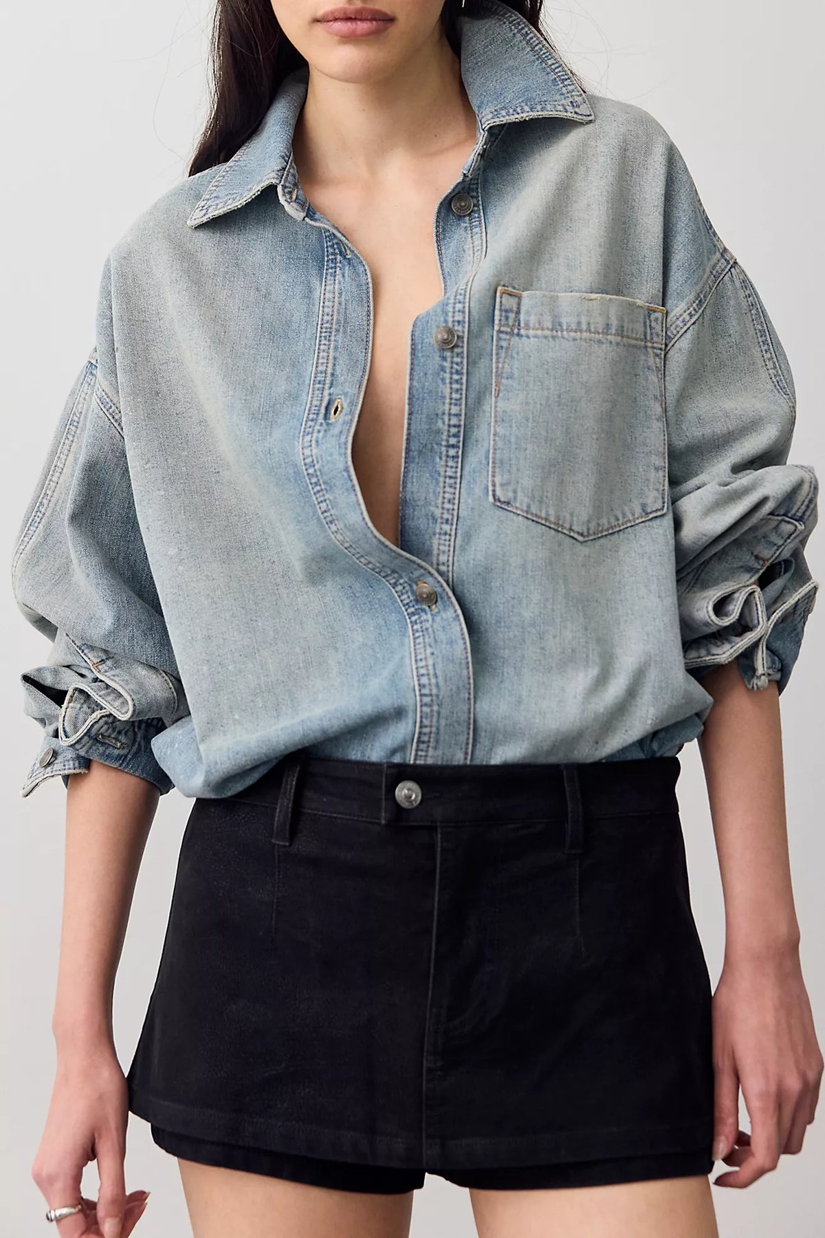 Close-up of black vegan suede micro skort with zip fly and offset button, styled with a light-wash denim shirt