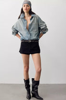 Model wearing We The Free Gallivanting skort in black vegan suede with a chambray shirt and black knee boots, full-length front view