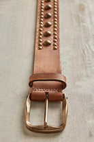 Close-up of cognac leather belt with rounded studs and antiqued brass-tone buckle